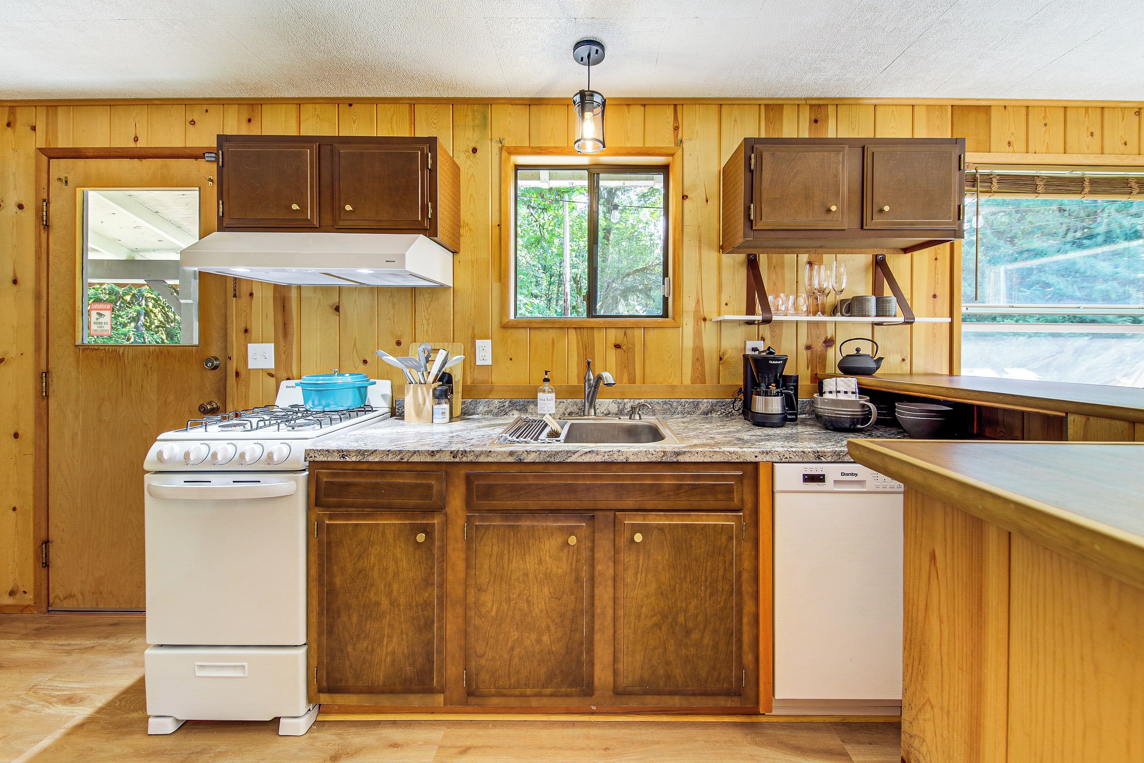 Una cocina con armarios de madera, estufa, lavamanos y ventana con vista a árboles.