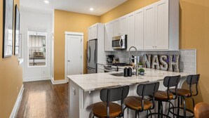 A modern kitchen with white cabinets, a marble island, and bar stools. - Private Rooftop, Near Vanderbilt, only 2 Miles from Downtown (Nashville)
