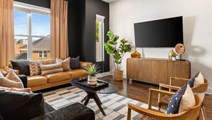 A modern living room with a leather sofa, a wooden coffee table, and a large flat-screen TV mounted on the wall. - Private Rooftop, Near Vanderbilt, only 2 Miles from Downtown (Nashville)