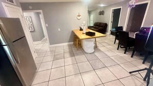 A kitchen with a refrigerator, a wooden table, and a dining area with chairs.
