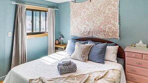 A bedroom with a bed, a dresser, a nightstand, and a window with curtains.