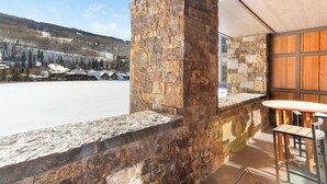 Un muro di pietra con un tavolo e sedie di legno, affacciato su un paesaggio innevato con edifici in lontananza.