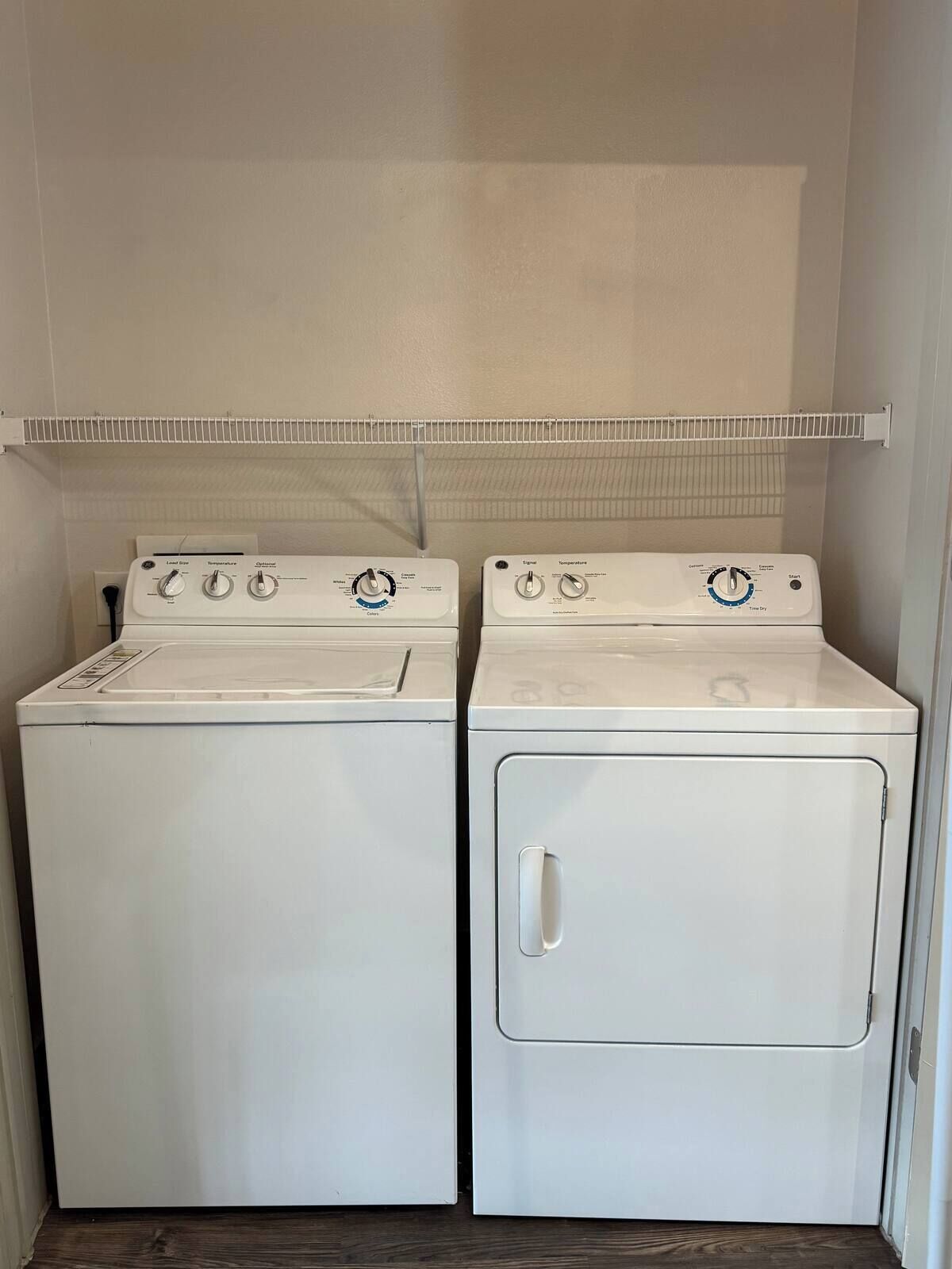 Une buanderie équipée de deux machines à laver et deux sèche-linge superposés, une étagère en métal au-dessus et un plancher en bois.