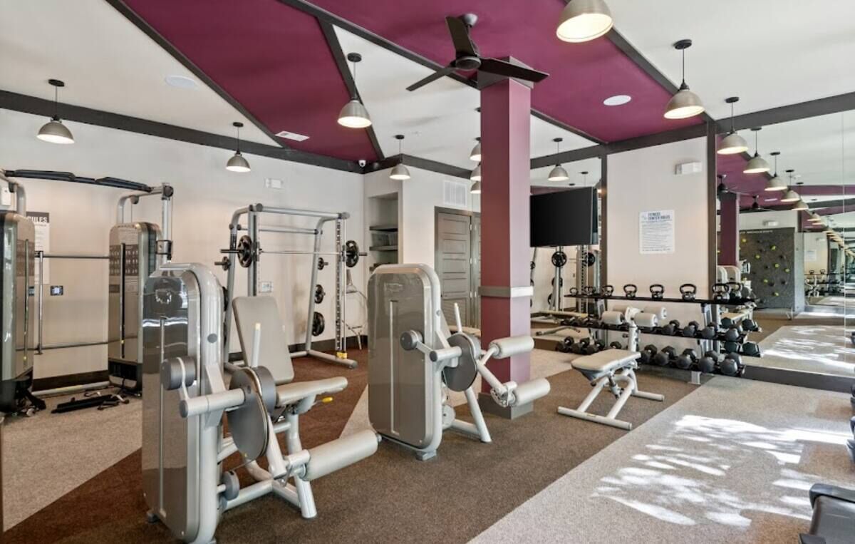 Un gimnasio con diversas máquinas de ejercicio, espejos y pesas.