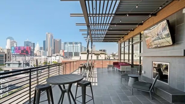 Una terraza en la azotea con vistas a la ciudad, una mesa con sillas y un televisor montado en la pared.