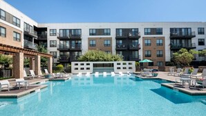 Un edificio moderno con piscina, sillas de descanso y una zona de estar cubierta.