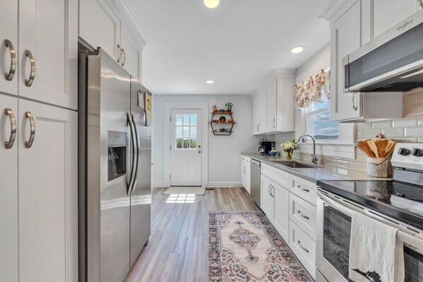 A modern kitchen with white cabinetry, stainless steel appliances, and a patterned rug.