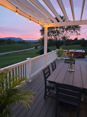 A wooden deck with a table and chairs, overlooking a grassy landscape and a pool area.