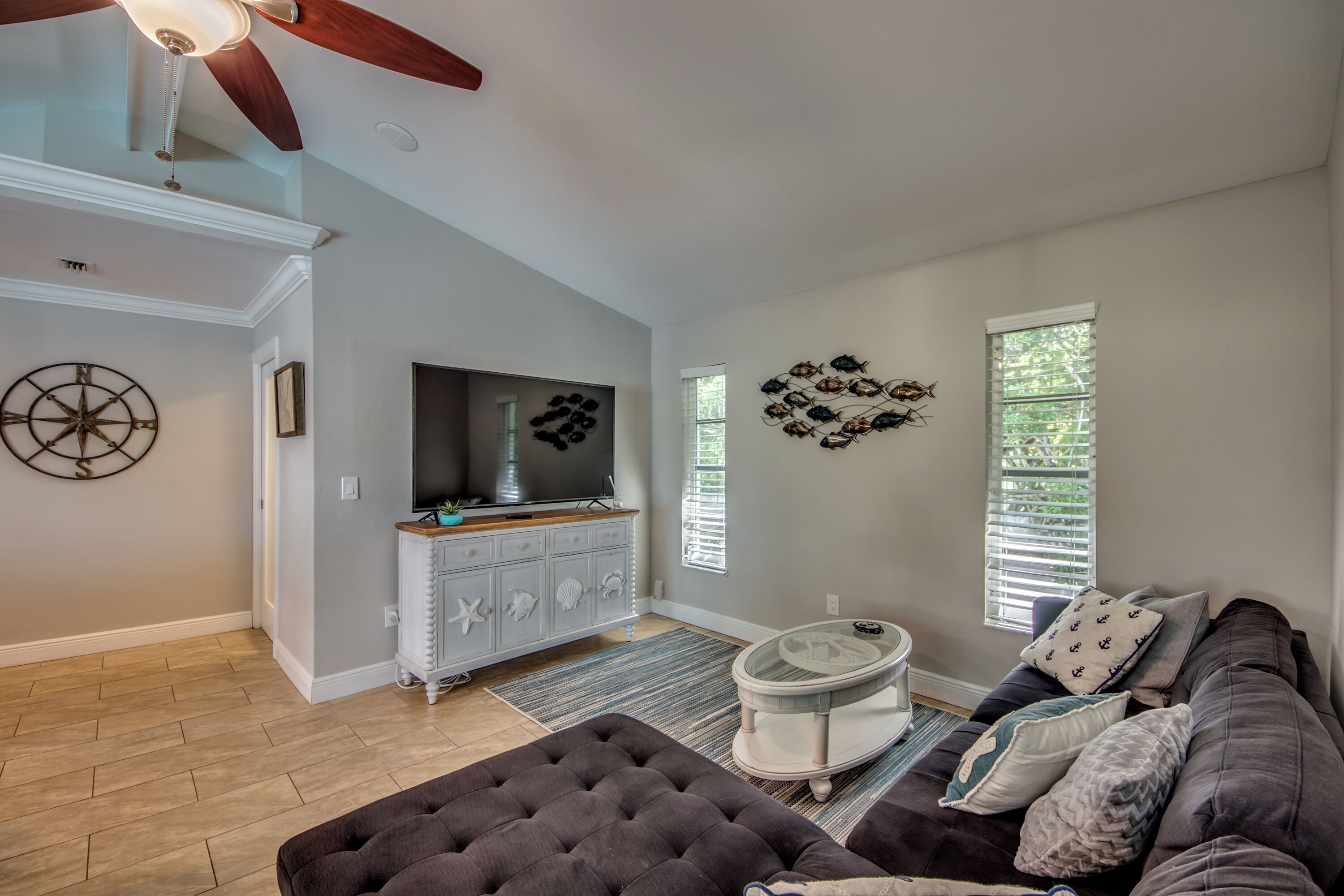 A living room with a television, a gray sofa, a round coffee table, and a ceiling fan.