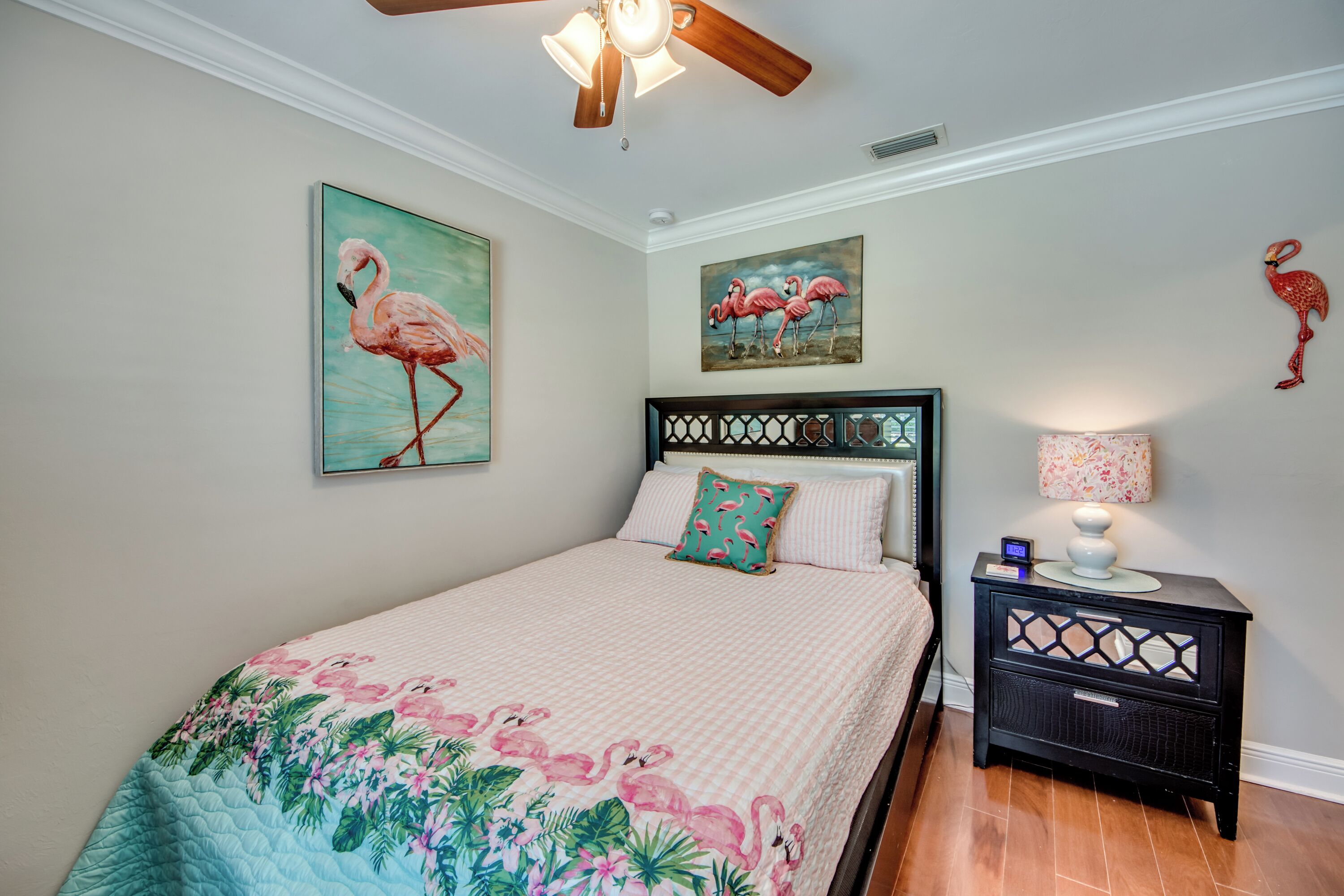 Ein Schlafzimmer mit einem Bett, einem Nachttisch und zwei an der Wand befestigten Flamingo-Bildern.