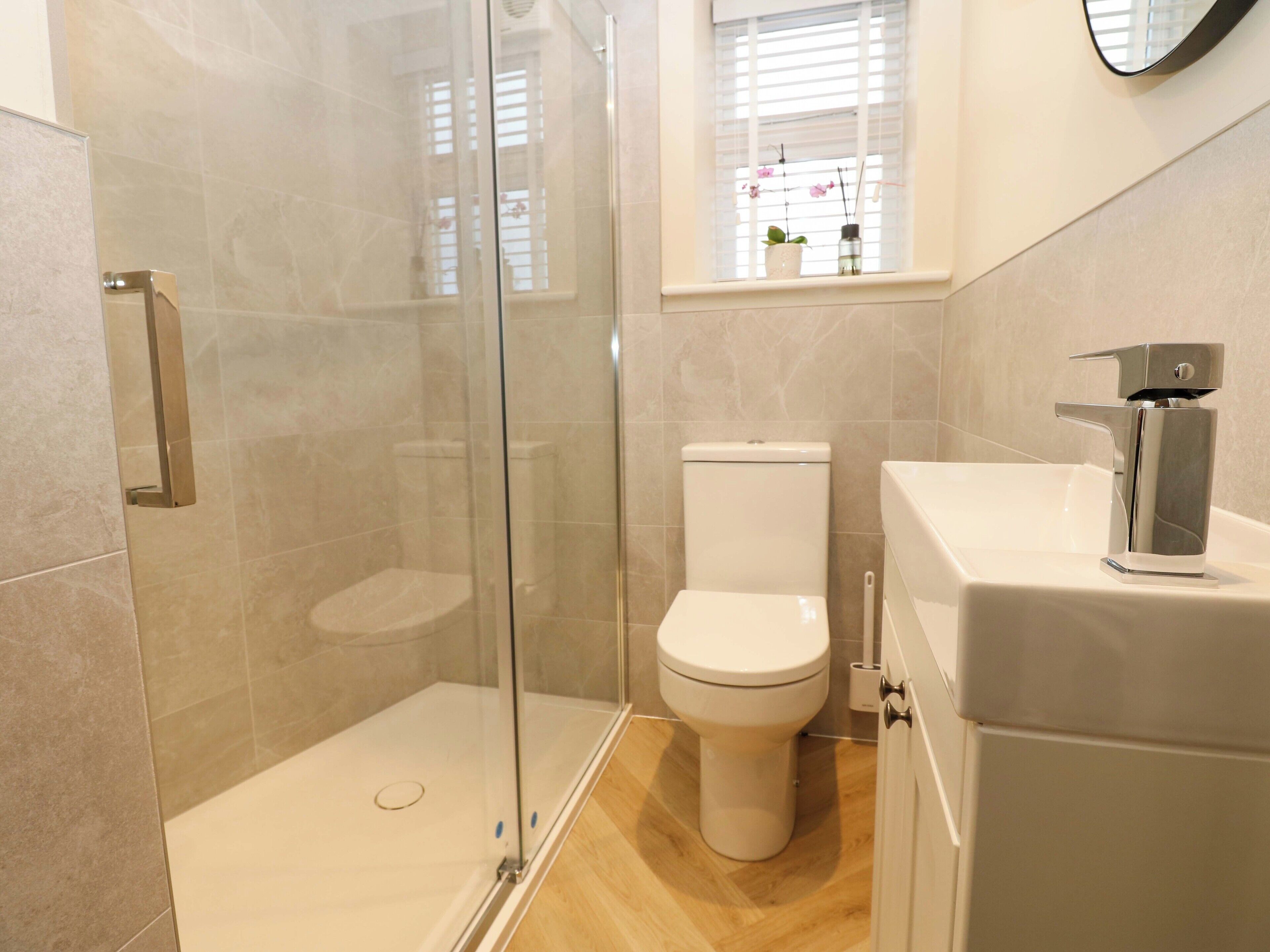 Un baño moderno con ducha de vidrio, inodoro blanco y lavamanos con grifo cromado.