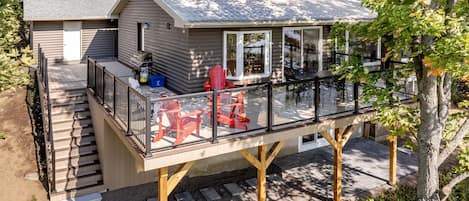 Eine zweistöckige Hütte mit Terrasse, Sitzgelegenheiten im Freien und einer Garage.