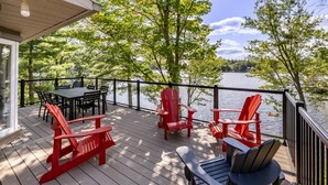 A wooden deck with outdoor seating, a table, and a view of a lake.