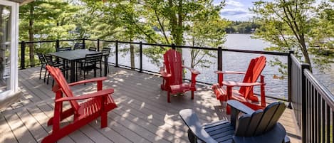 Una terraza de madera con mobiliario exterior, una mesa y vista a un lago.
