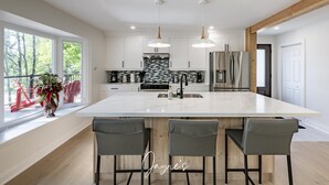 A modern kitchen with a large island, white cabinetry, stainless steel appliances, and pendant lighting.