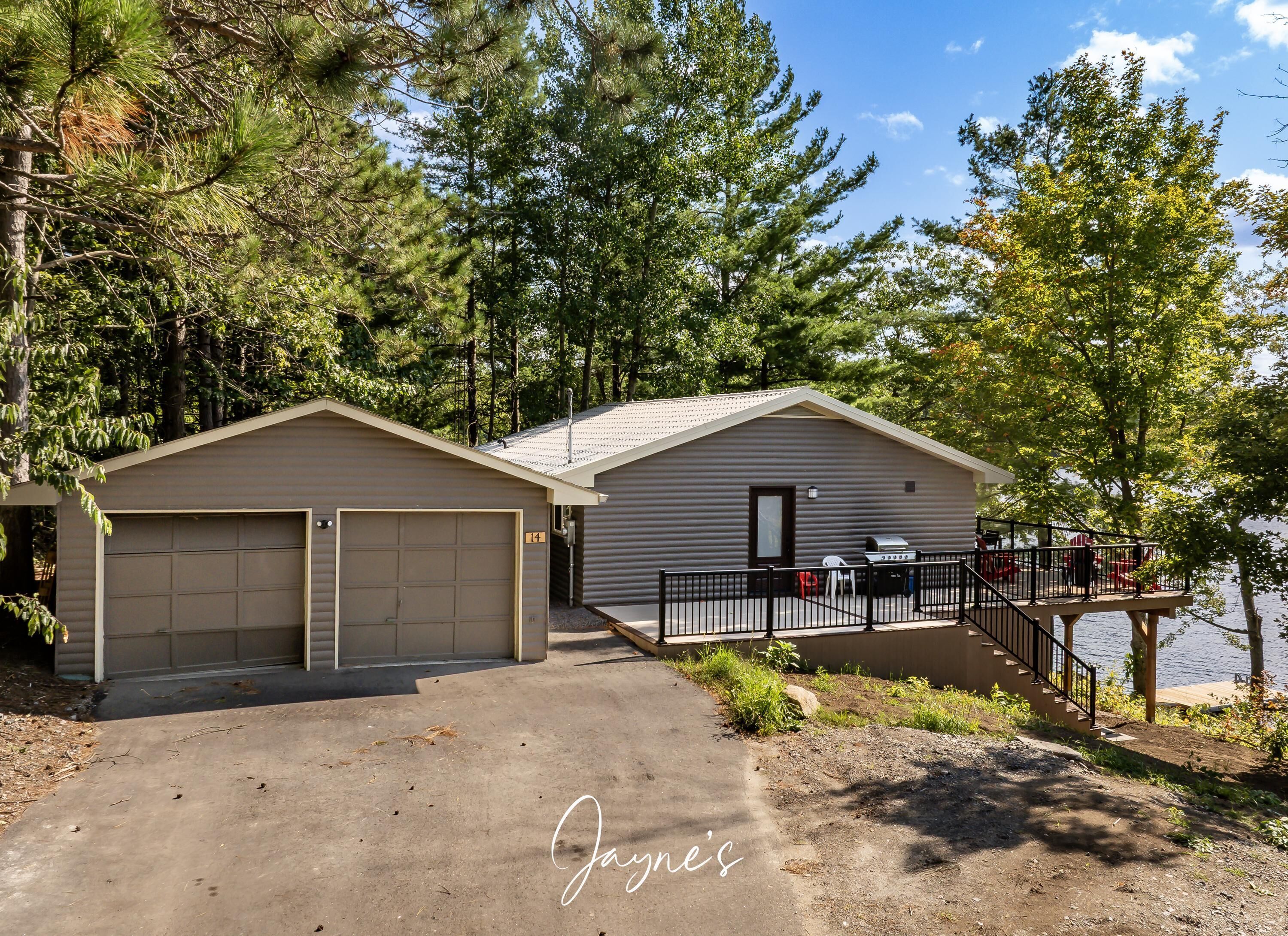A cabin with two garage doors, a deck with outdoor seating, and a view of the lake.