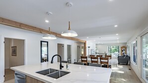 A modern kitchen with a large island, wooden cabinets, and a dining area with a table and chairs.