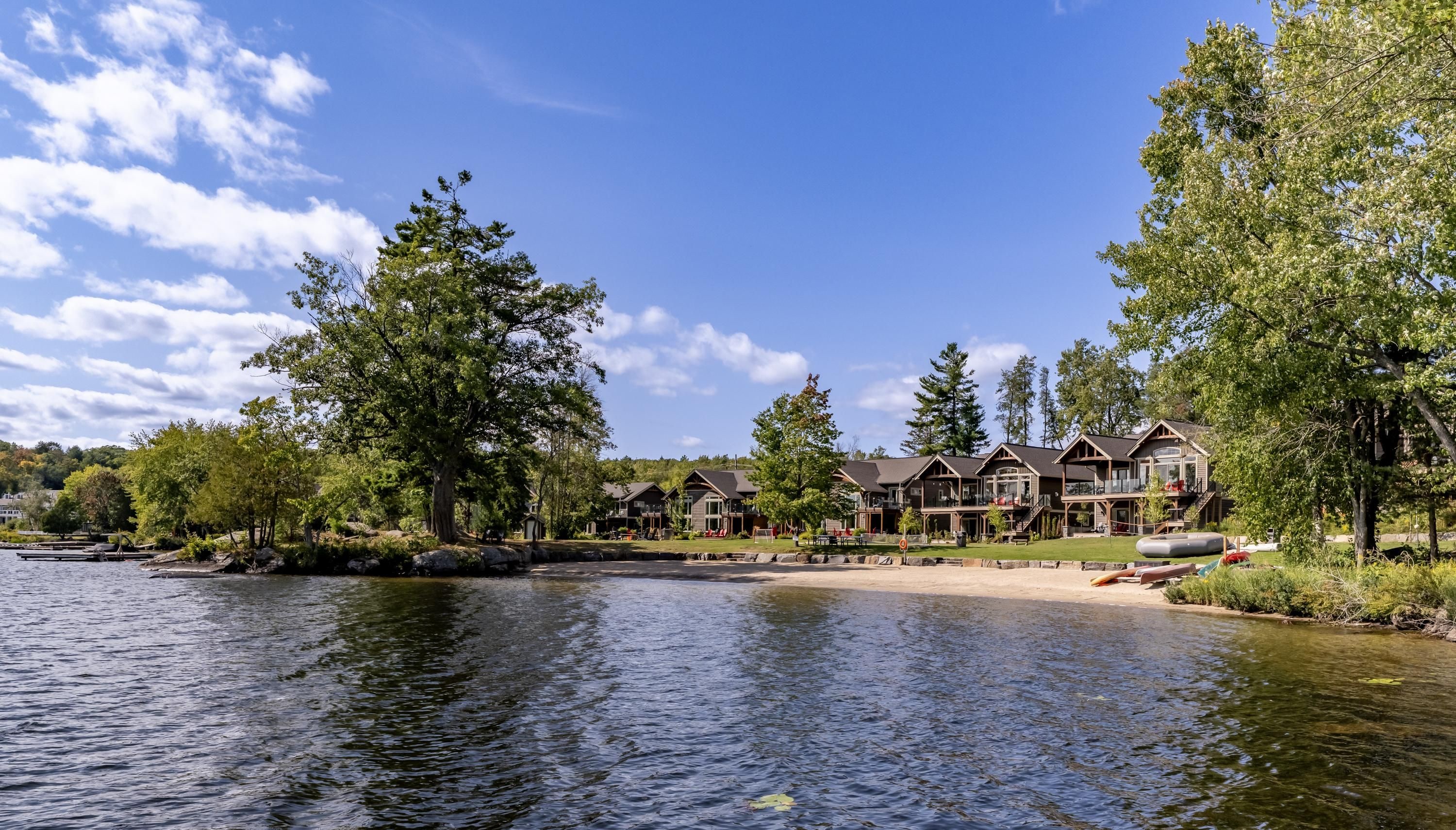 Un resort junto al lago con varias cabañas de madera, una playa de arena y un lago tranquilo.