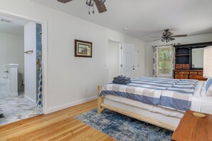 A bedroom with a bed, a ceiling fan, a wooden floor, and a door leading to a bathroom.