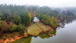 A house with a dock extending into a lake, surrounded by autumn-colored trees.