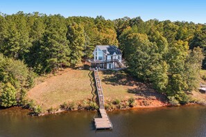 A house with a dock leading to a lake surrounded by dense forest.