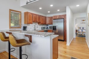 A modern kitchen with a central island, wooden cabinets, stainless steel appliances, and a bar stool seating area.