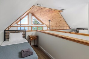A bedroom with a sloped ceiling, a bed with a wooden headboard, a bedside table, and a window with a view of trees.