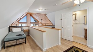 A loft bedroom with a sloped ceiling, wooden beams, a bed, a small table, and a ceiling fan.