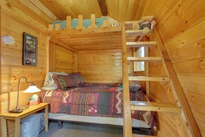 Una camera in una baita di legno con un letto a castello, una scrivania con una lampada e un quadro appeso al muro.
