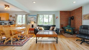 A spacious living room with a wooden dining table, comfortable seating, a fireplace, and large windows offering a view of the outdoors. - Mtn Views, On-Site Trails! Spacious Bartlett Home (Bartlett)