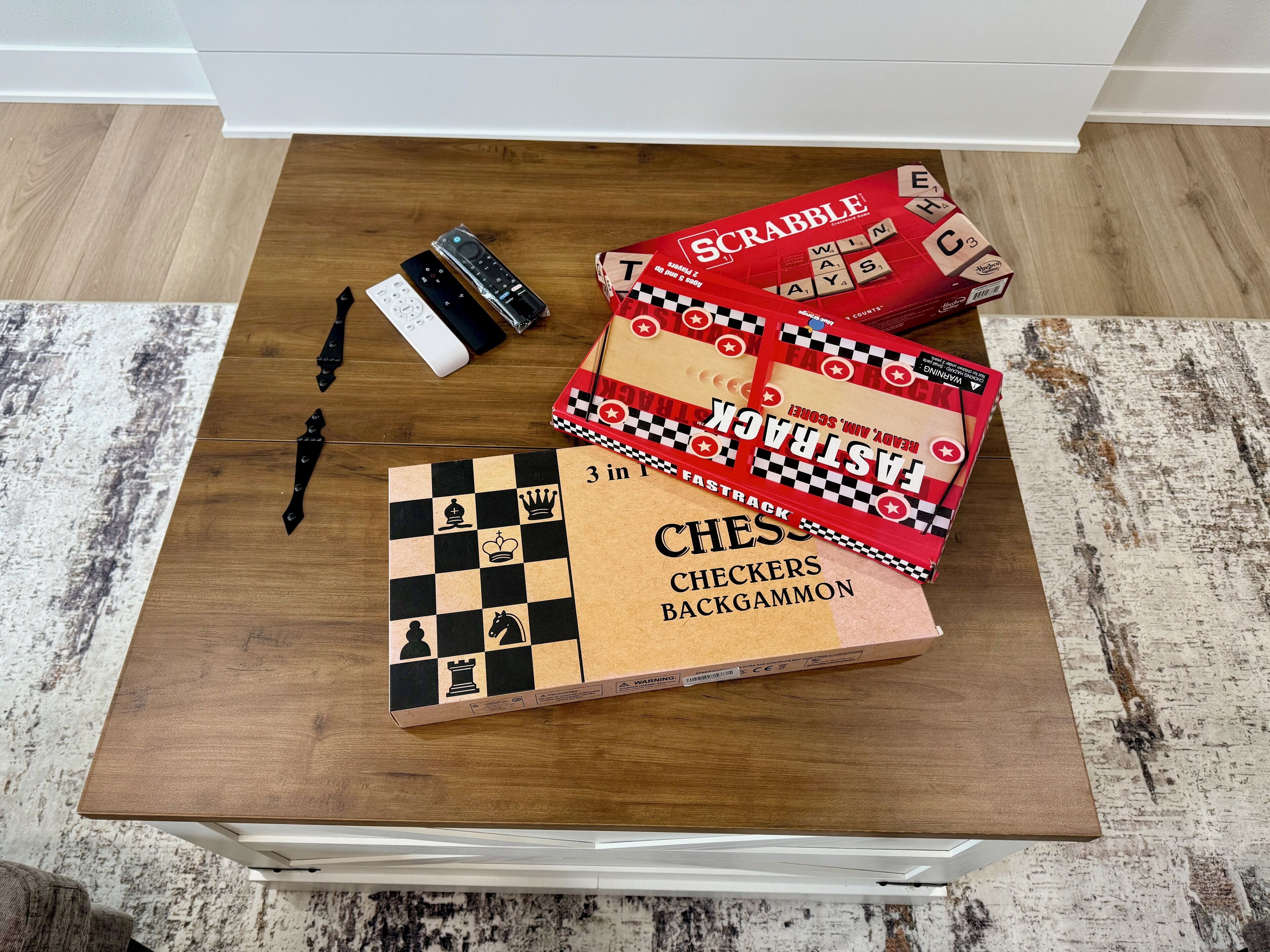 A wooden table with a chessboard, Scrabble tiles, and a remote control.