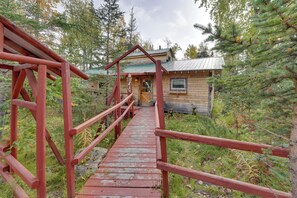 Una cabaña de madera con techo de metal, accesible por un puente de madera con barandillas rojas.