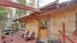 Eine Holzhütte mit Veranda, Grill, Gartenmöbeln und einer Tür mit Fensterteil.