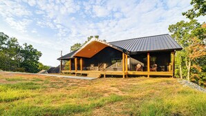 A modern house with a large deck, surrounded by a grassy field and trees. - Private Beach on Lake Barkley! Scenic Family Oasis (Cadiz)