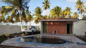 A swimming pool with a brick patio, a white SUV parked nearby, and palm trees in the background. - Cozy beach house with pool, in Aver o Mar, year-round sunshine. (Barra do Sirinhaém)
