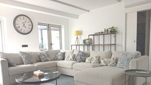 Ein modernes Wohnzimmer mit einer Eckcouch, einem Glastisch, einer Uhr und einem Bücherregal.