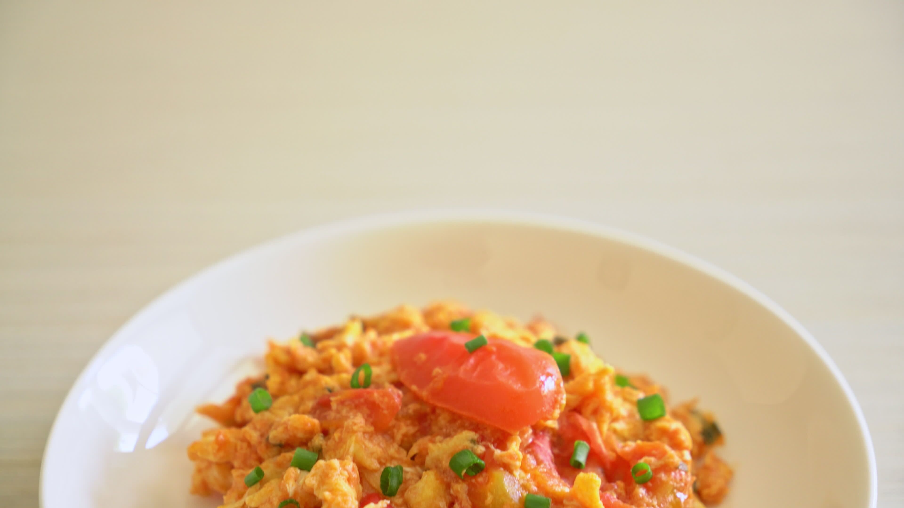 A white bowl with scrambled eggs, a slice of tomato, and green onions.