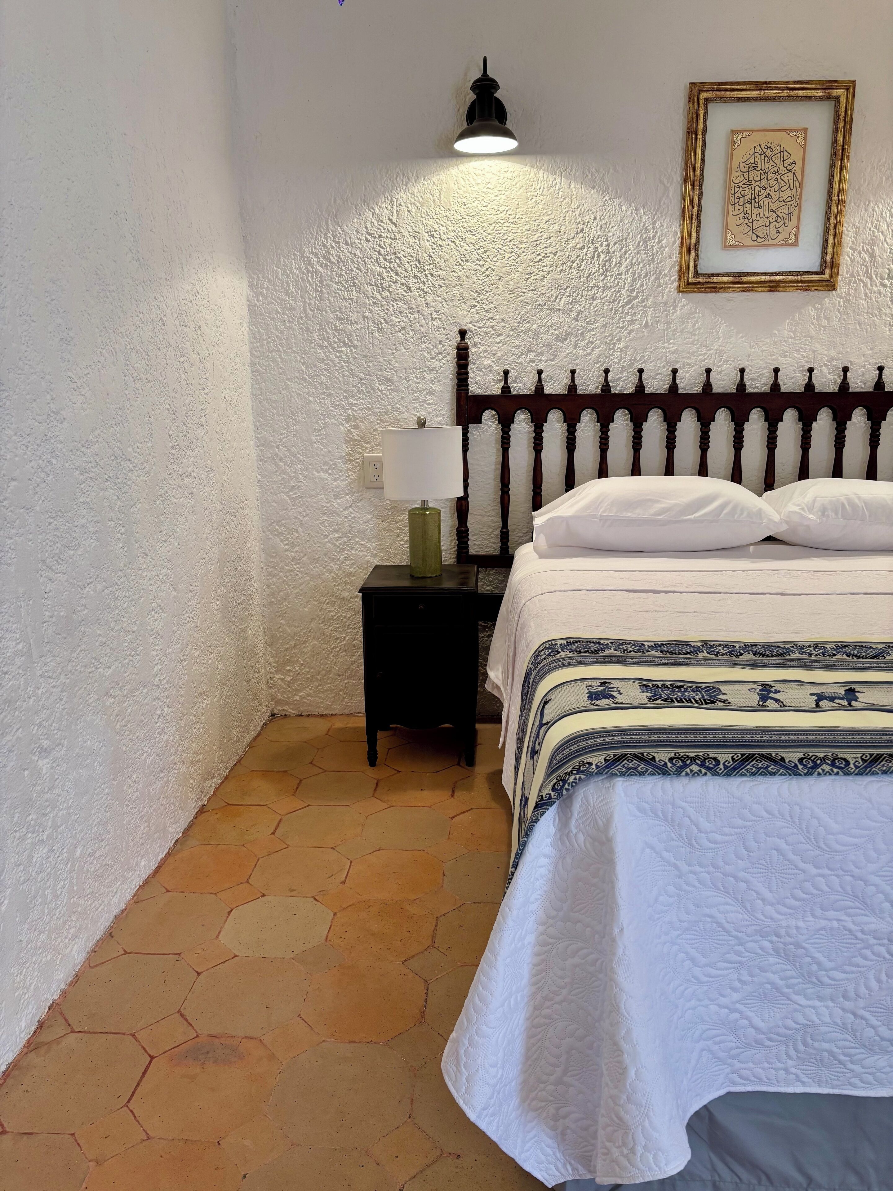 A neatly made bed with a patterned bedspread, a bedside lamp, and a framed artwork on the wall.