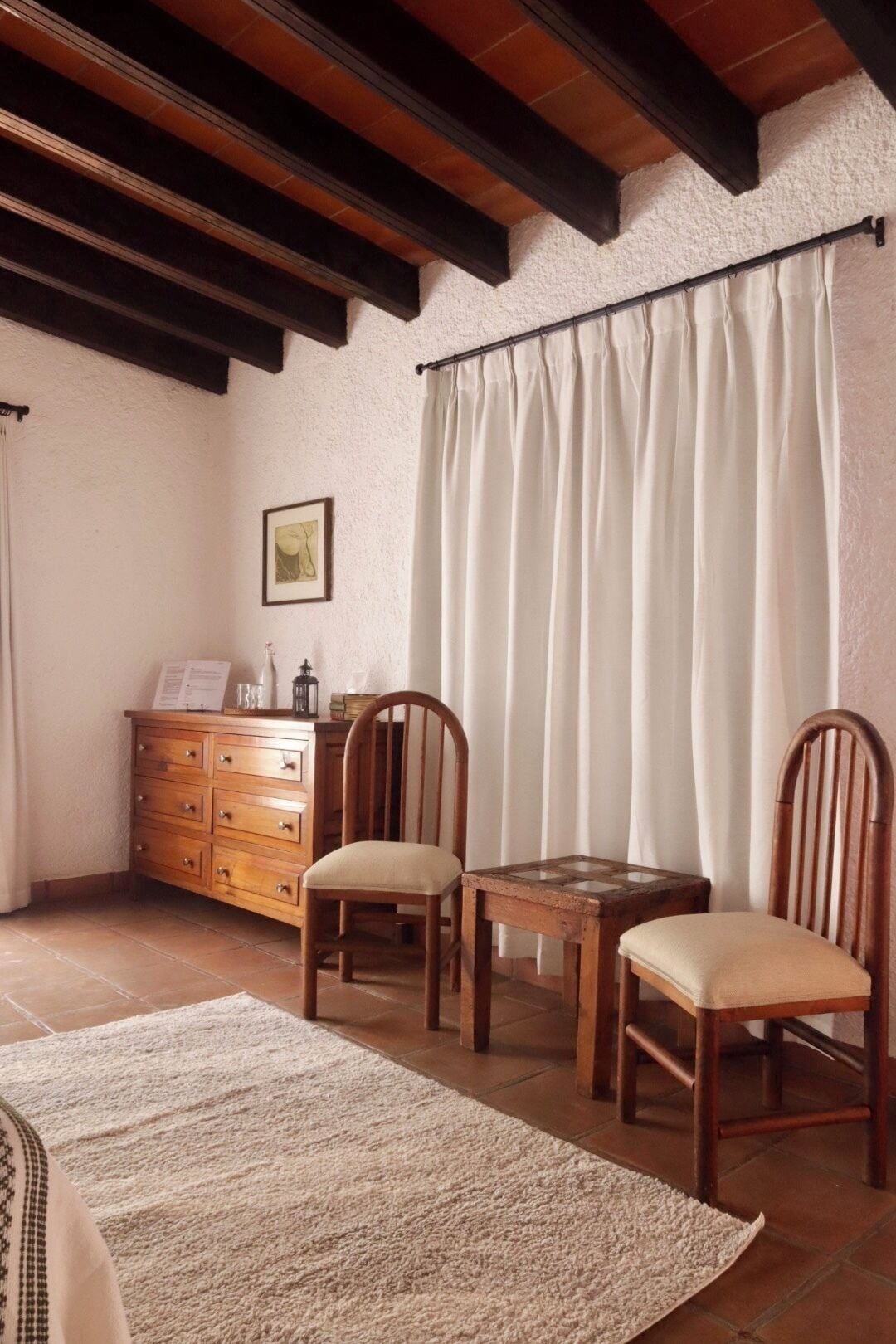 Una habitación acogedora con una mesa y sillas de madera, un armario y un ventanal con cortinas.