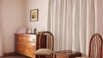 Una habitación acogedora con una mesa y sillas de madera, un armario y un ventanal con cortinas.