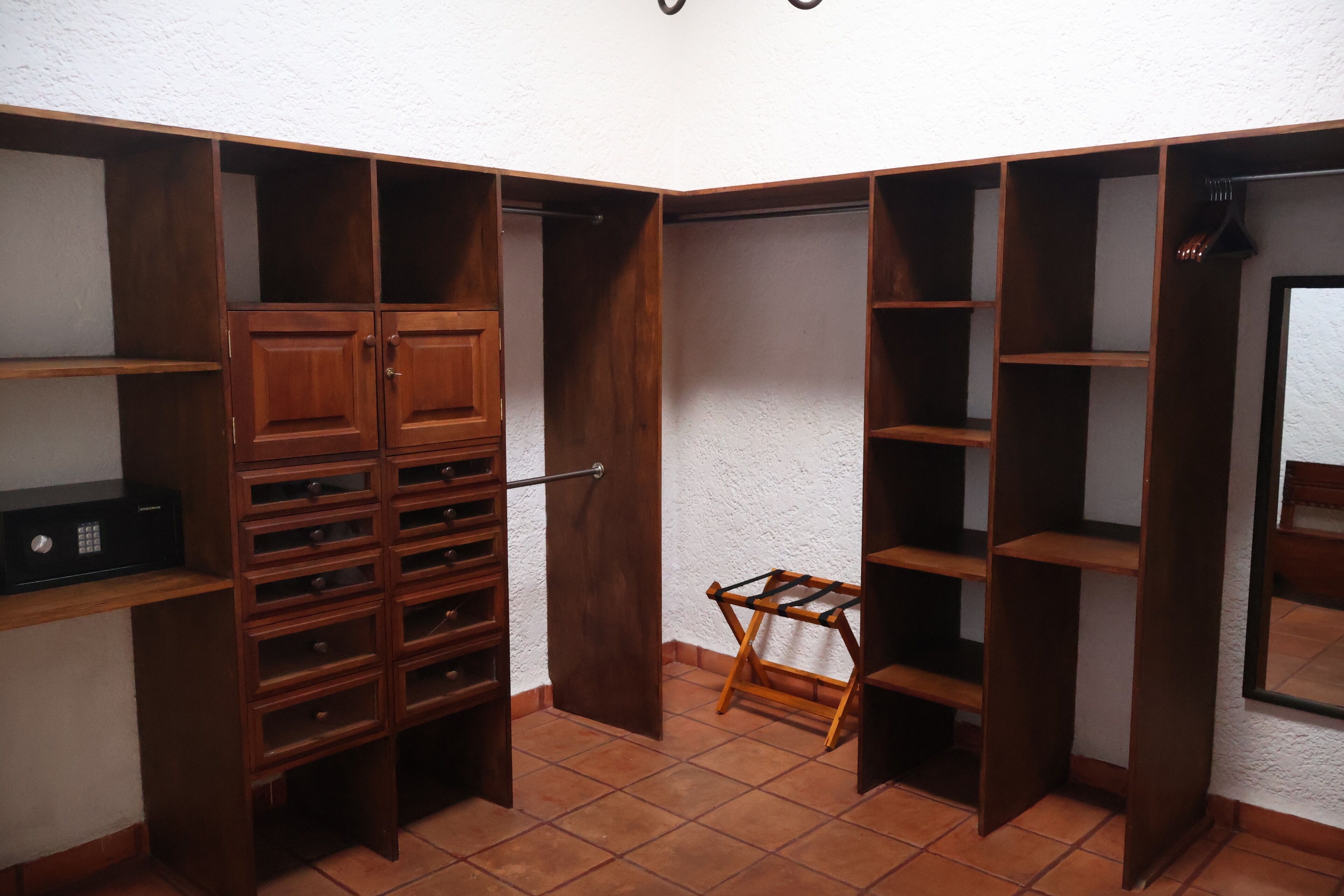 Un armario de esquina con varios estantes y cajones de madera, una barra para colgar ropa y un dispositivo electrónico negro a la izquierda.