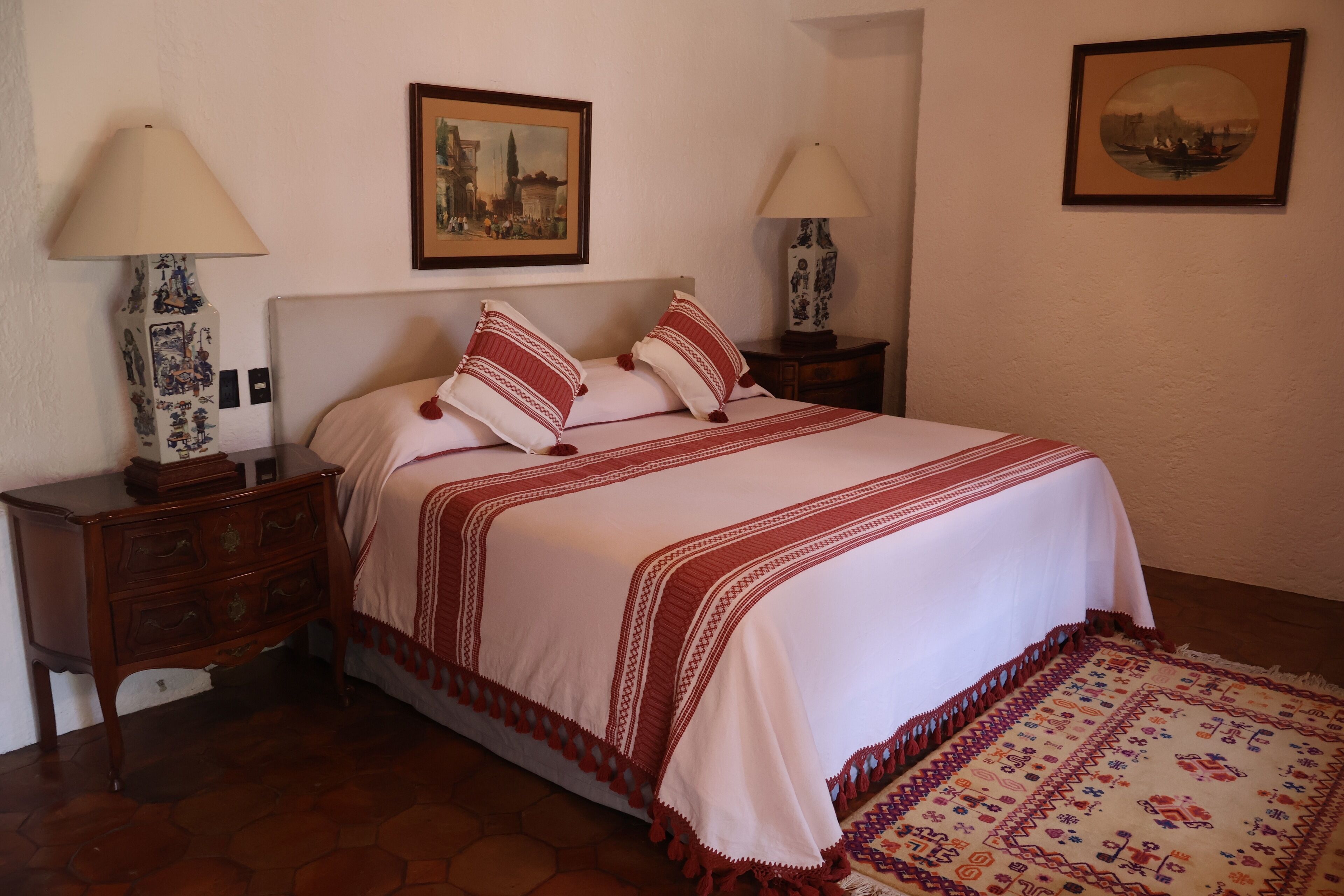 A neatly arranged bedroom with a bed, two bedside tables, two lamps, and two framed pictures on the wall.