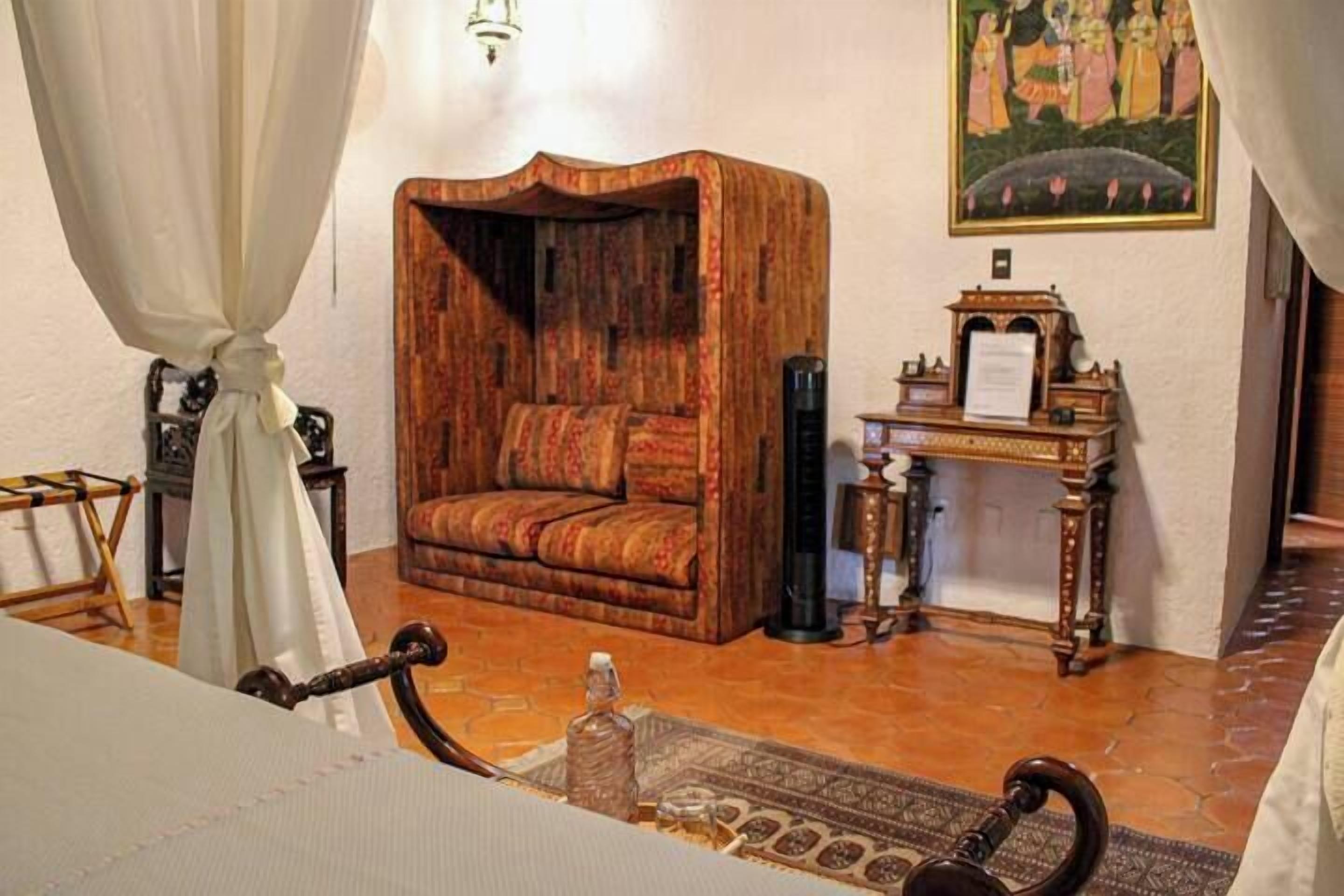A traditional room with a wooden sofa, a small table with a lamp, and a painting on the wall.