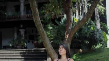 A person sitting on a yoga mat outdoors with a building and trees in the background.