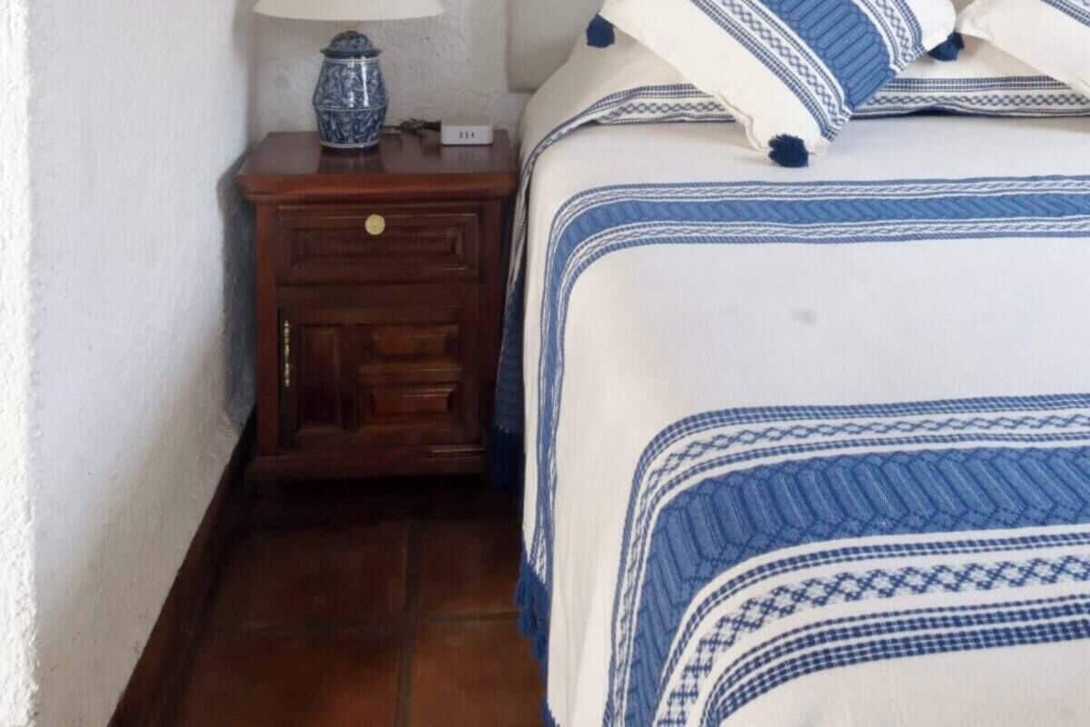 Ein Schlafzimmer mit einem Bett, einem Nachttisch, einer Lampe und einem gerahmten Gegenstand an der Wand.
