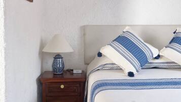 Un dormitorio con cama, mesita de noche, lámpara y un objeto enmarcado en la pared.