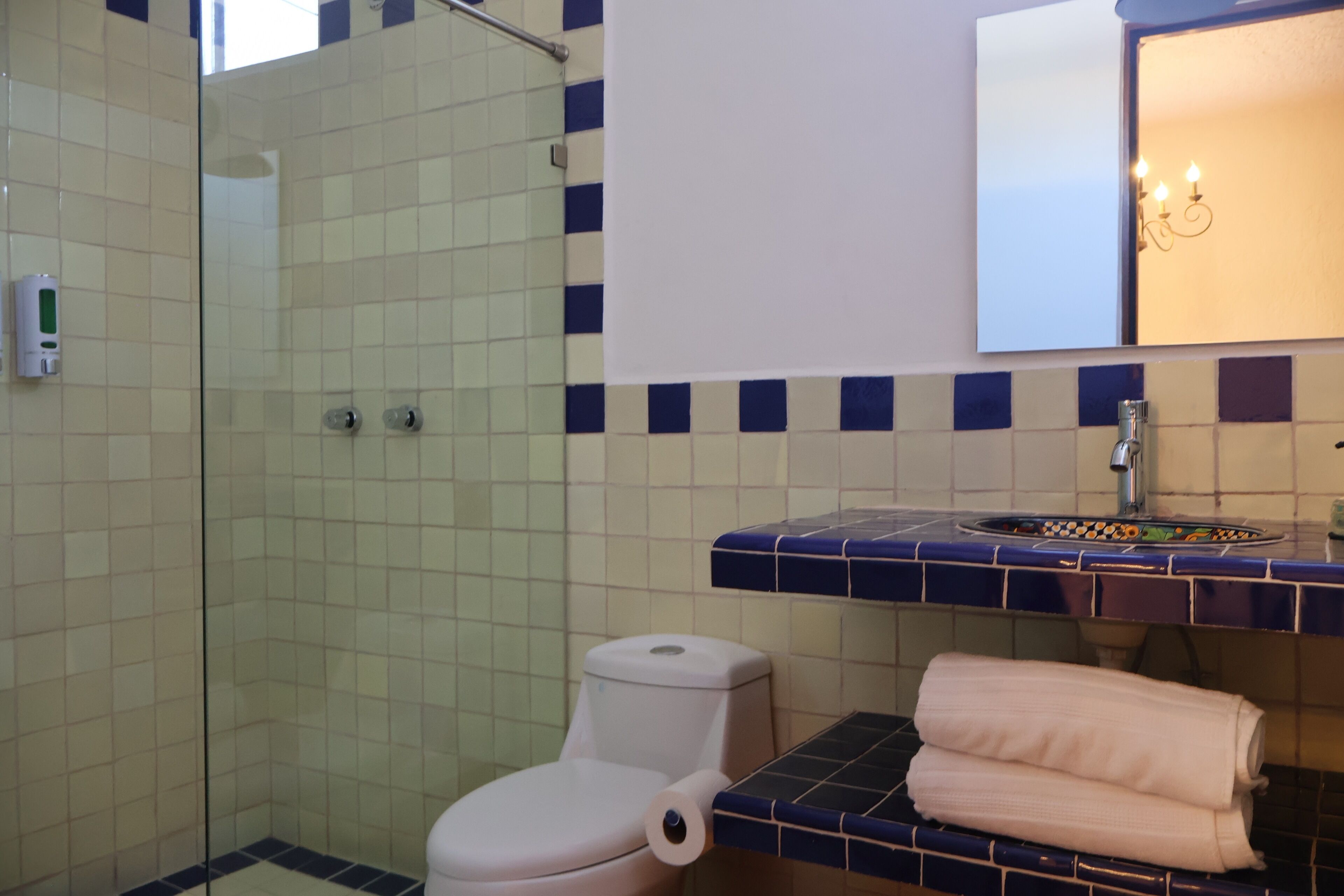 Un baño con cabina de ducha de vidrio, inodoro, lavamanos con encimera azul de azulejos y toallero con toallas.