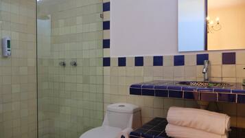 Un baño con cabina de ducha de vidrio, inodoro, lavamanos con encimera azul de azulejos y toallero con toallas.