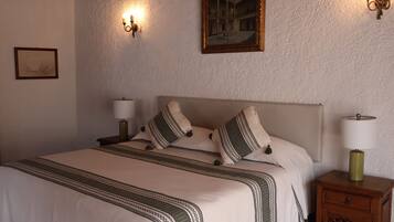 Una cama bien hecha con una colcha estampada, dos lámparas de noche y una mesita de noche de madera con un cajón.