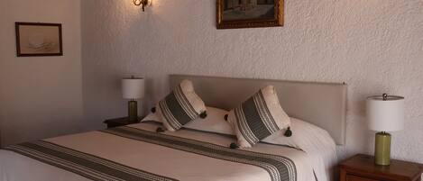A neatly made bed with a patterned bedspread, two bedside lamps, and a small wooden nightstand with a drawer.